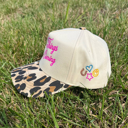 Beige cap with leopard print brim and colorful text and symbols on grass