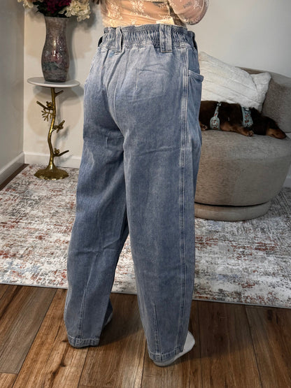 Person wearing blue jeans standing in a room with a couch and decorative items.