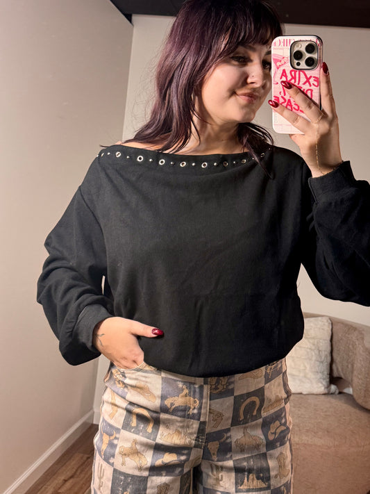 Black boat neck sweatshirt with silver metal studs, worn by a person with long sleeves and relaxed fit.