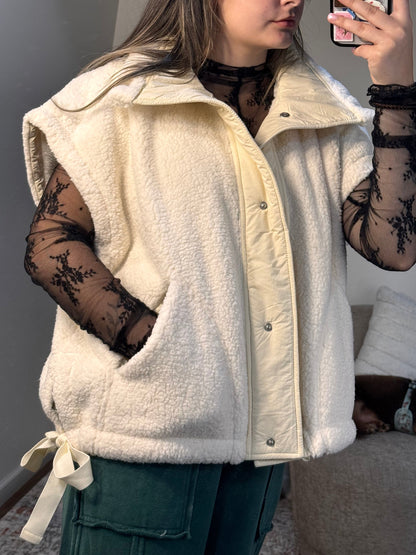 Person wearing a white coat with black lace sleeves and gloves, standing indoors.