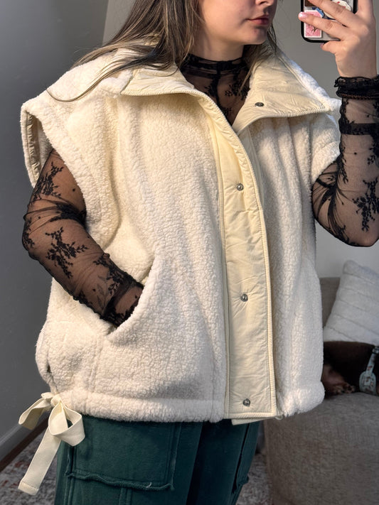 Person wearing a white coat with black lace sleeves and gloves, standing indoors.