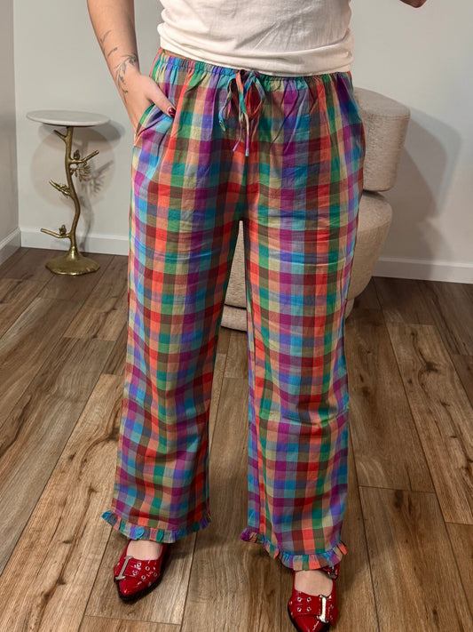 Multicolor plaid pants with a ruffle hem and elastic waistband, shown on a person standing indoors.