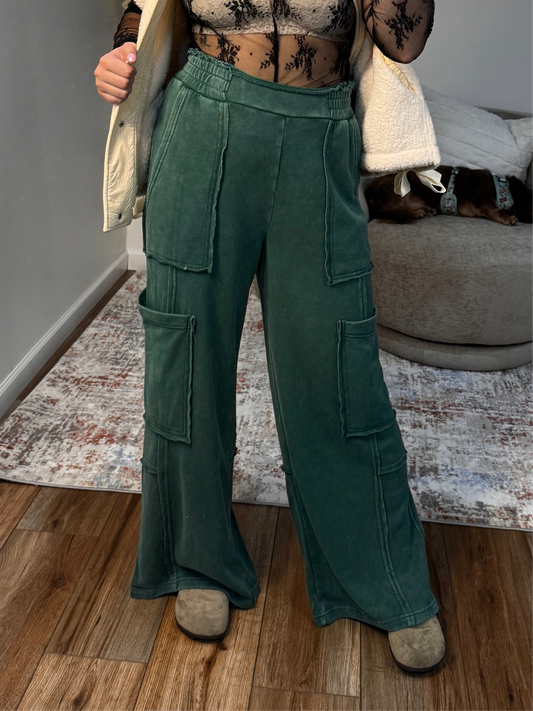 Person wearing green cargo pants standing on a wooden floor with a neutral background.