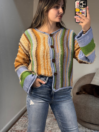 Person wearing a colorful striped sweater and jeans, taking a mirror selfie.