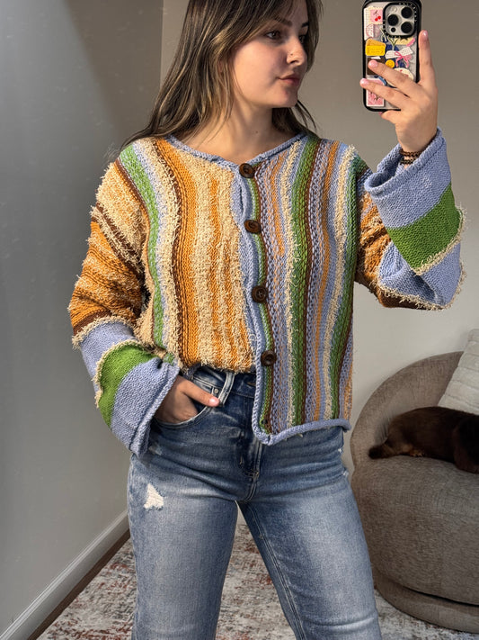Person wearing a colorful striped sweater and jeans, taking a mirror selfie.