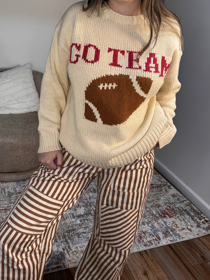 Person wearing a sweater with a football design and text indoors.