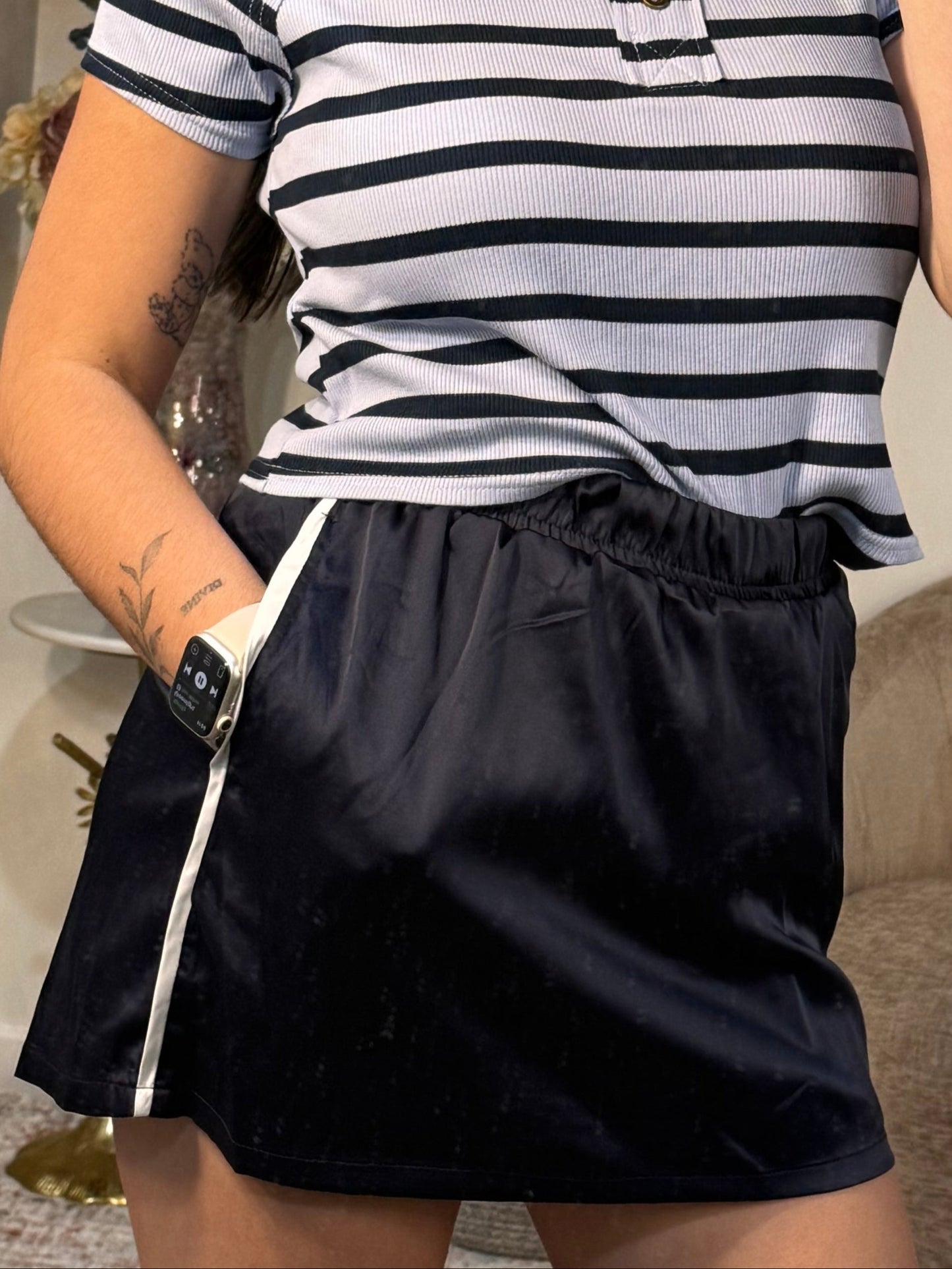 Person taking a mirror selfie wearing a striped shirt and black shorts in a room.
