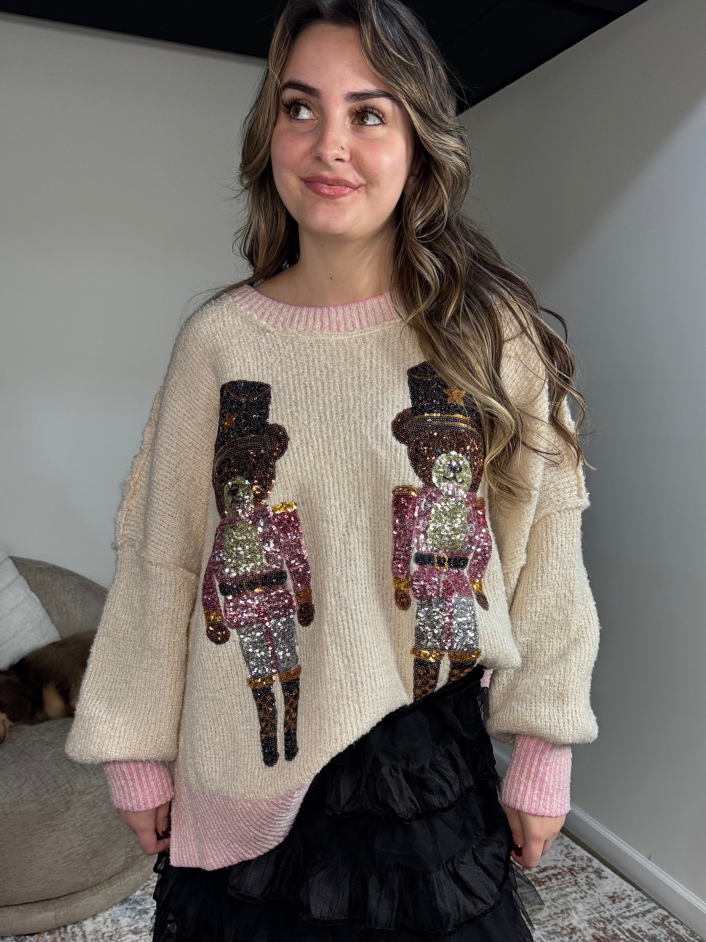 Woman wearing a beige sweater with sequin nutcracker designs in a room.