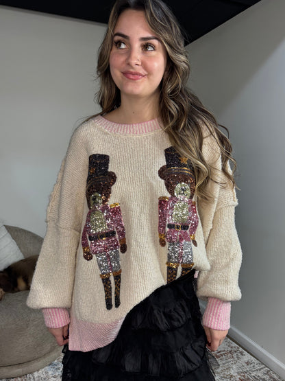 Woman wearing a beige sweater with sequin nutcracker designs in a room.