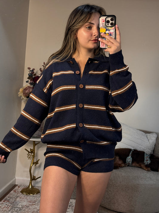 Person wearing a navy blue cardigan with gold stripes, taking a mirror selfie.