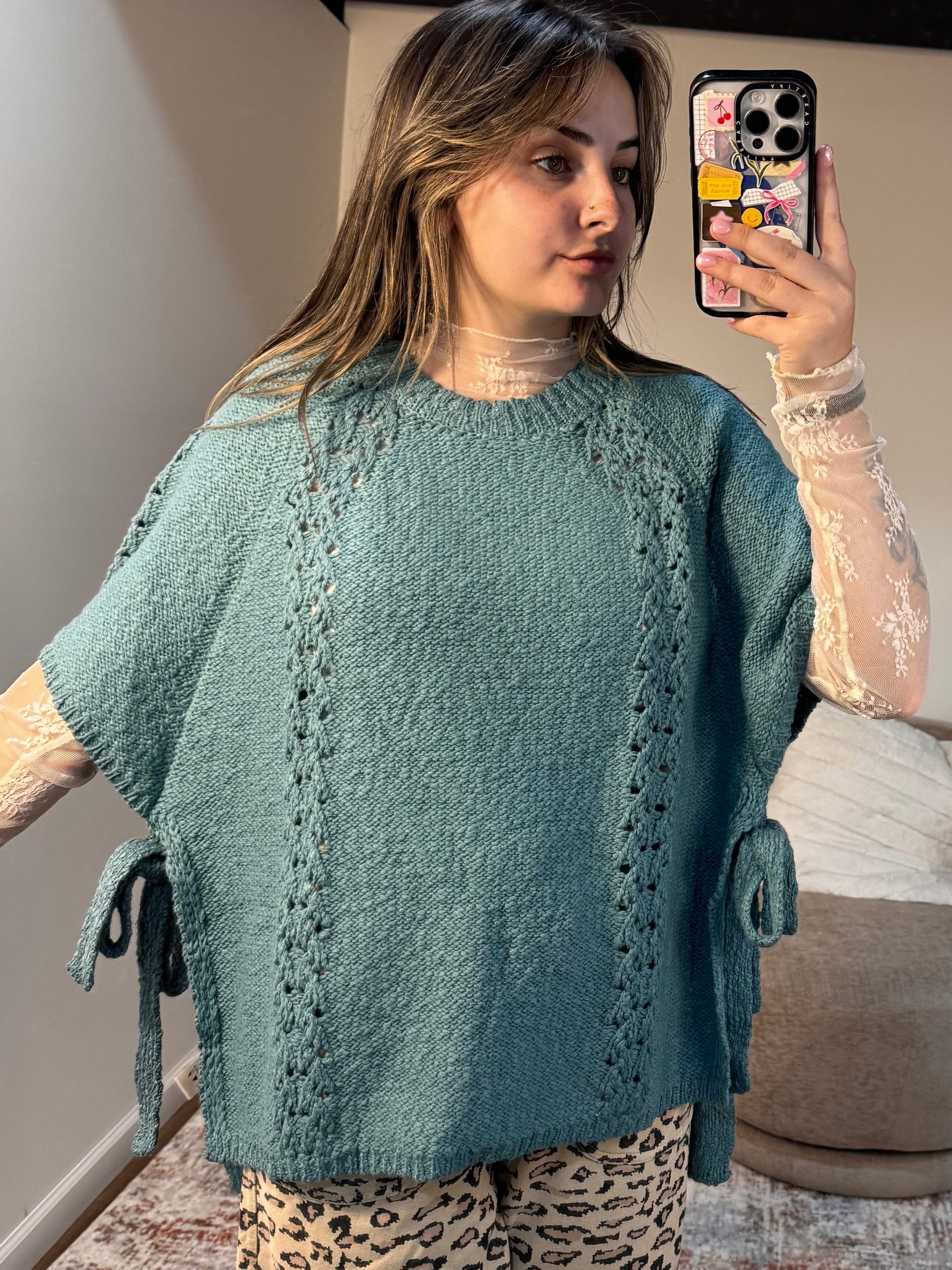 Woman taking a mirror selfie wearing a teal poncho in a living room.