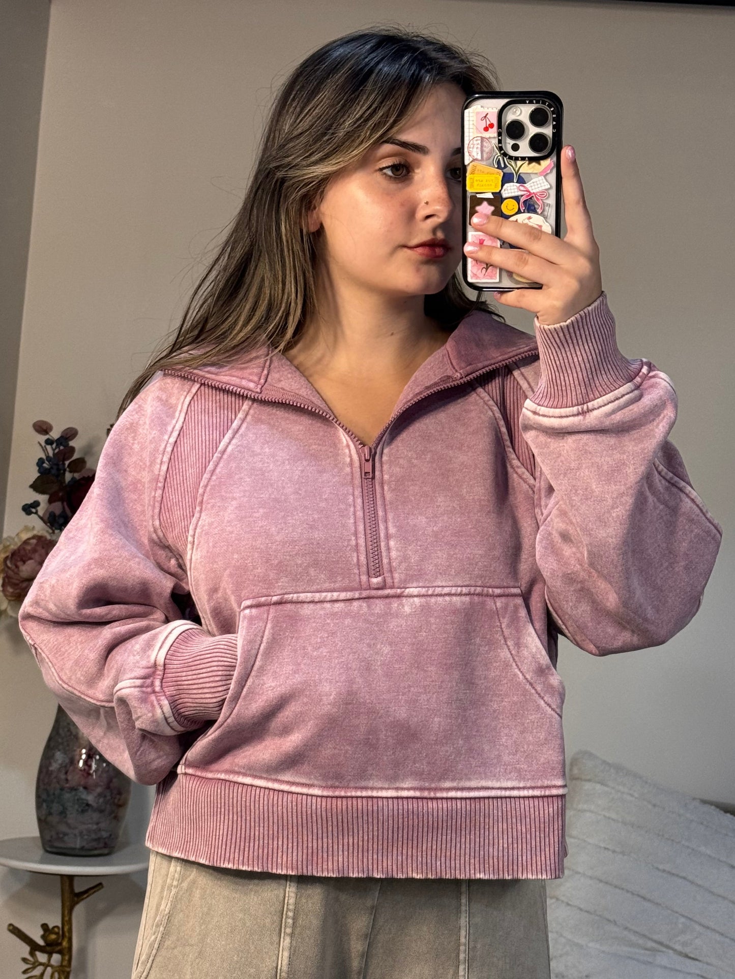 Person wearing a pink jacket taking a mirror selfie in a room.