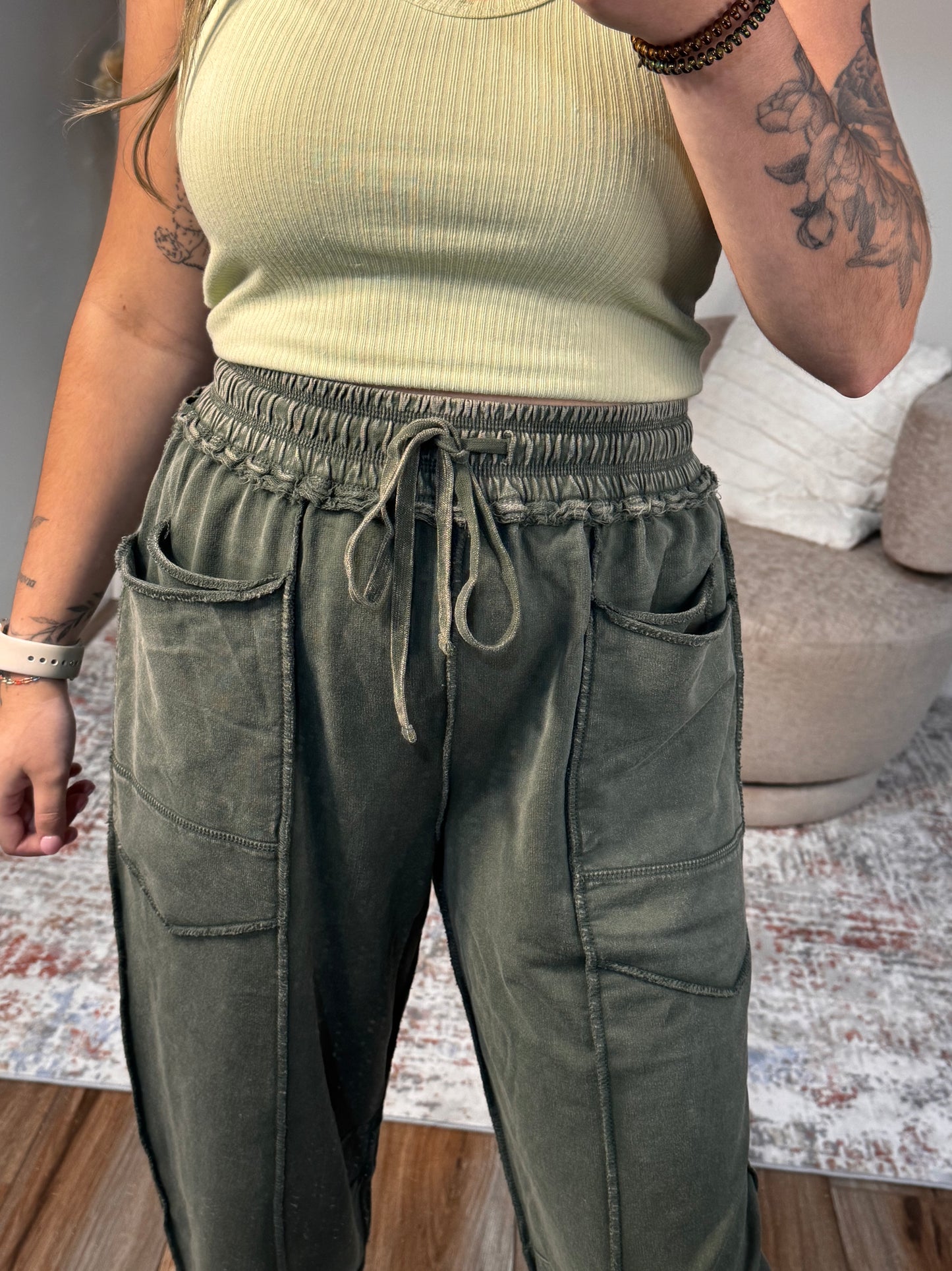 Person wearing green pants and a beige top with tattoos visible on arms.