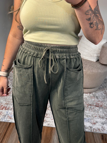 Person wearing green pants and a beige top with tattoos visible on arms.