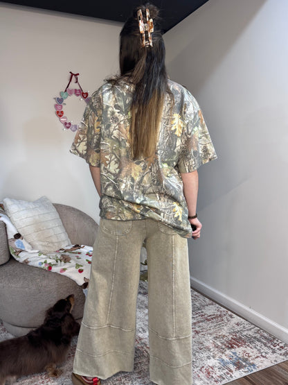 Person wearing a camouflage shirt and beige pants standing in a room with a couch and decorative items.