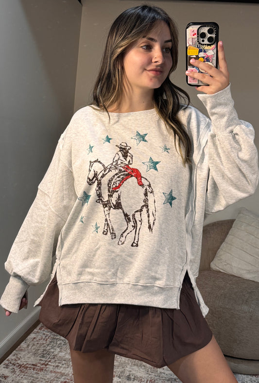 Woman wearing a gray sweatshirt with a horse and star design, taking a mirror selfie.