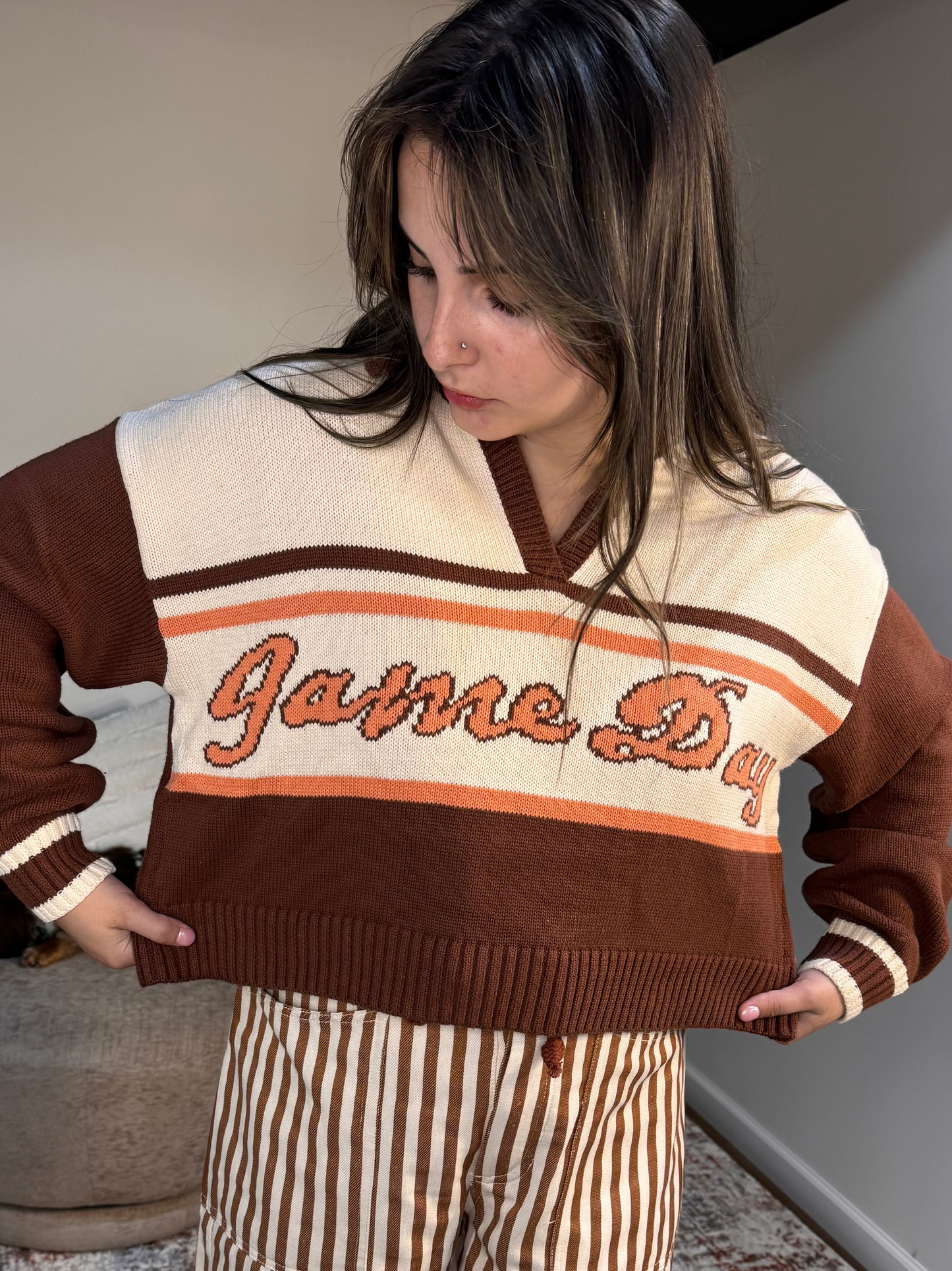 Woman wearing a brown and white sweater with 'Game Day' text, standing indoors.