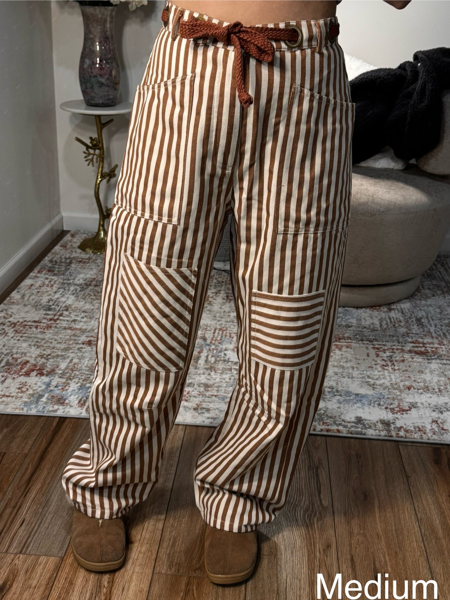 Person wearing brown and beige striped pants indoors on a wooden floor.